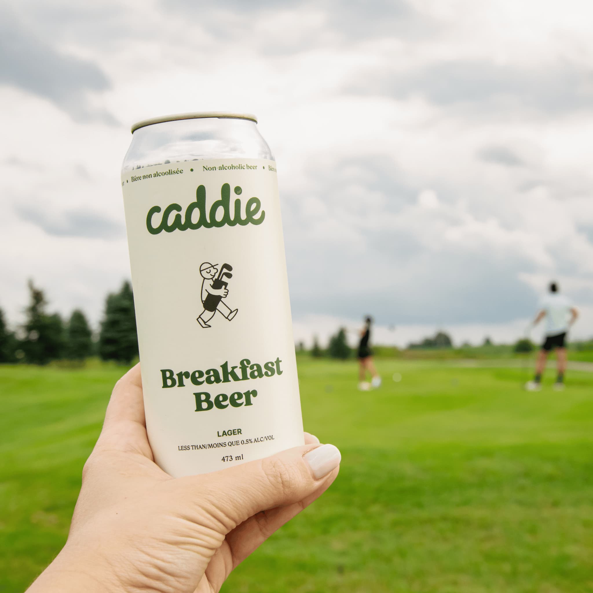 Caddie Breakfast Beer held with golfers teeing off in background